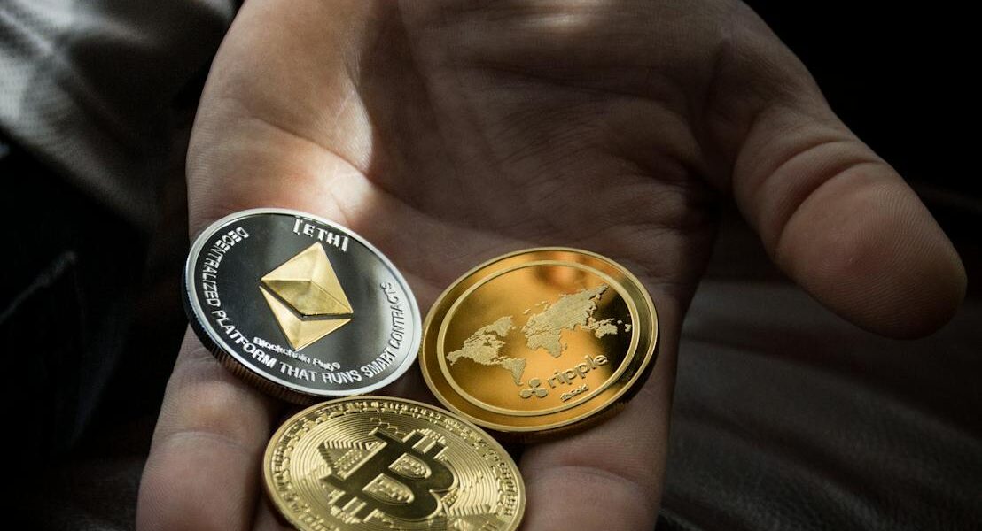 Hand holding Bitcoin, Ethereum, and Ripple coins representing digital currency.