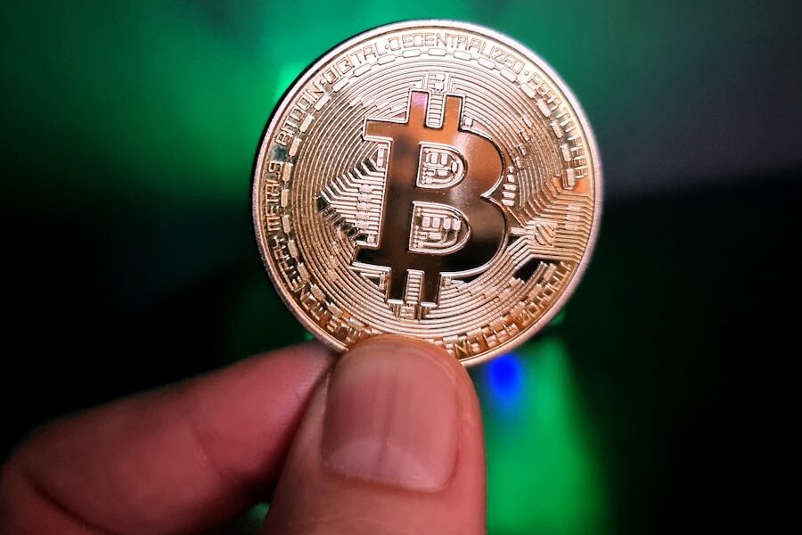 a hand holding a bit coin in front of a green light