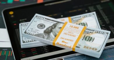 Stack of $100 bills placed on a tablet with financial graphs, symbolizing digital finance.