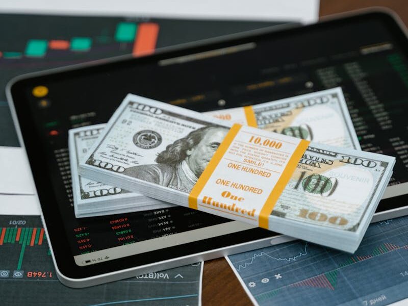 Stack of $100 bills placed on a tablet with financial graphs, symbolizing digital finance.