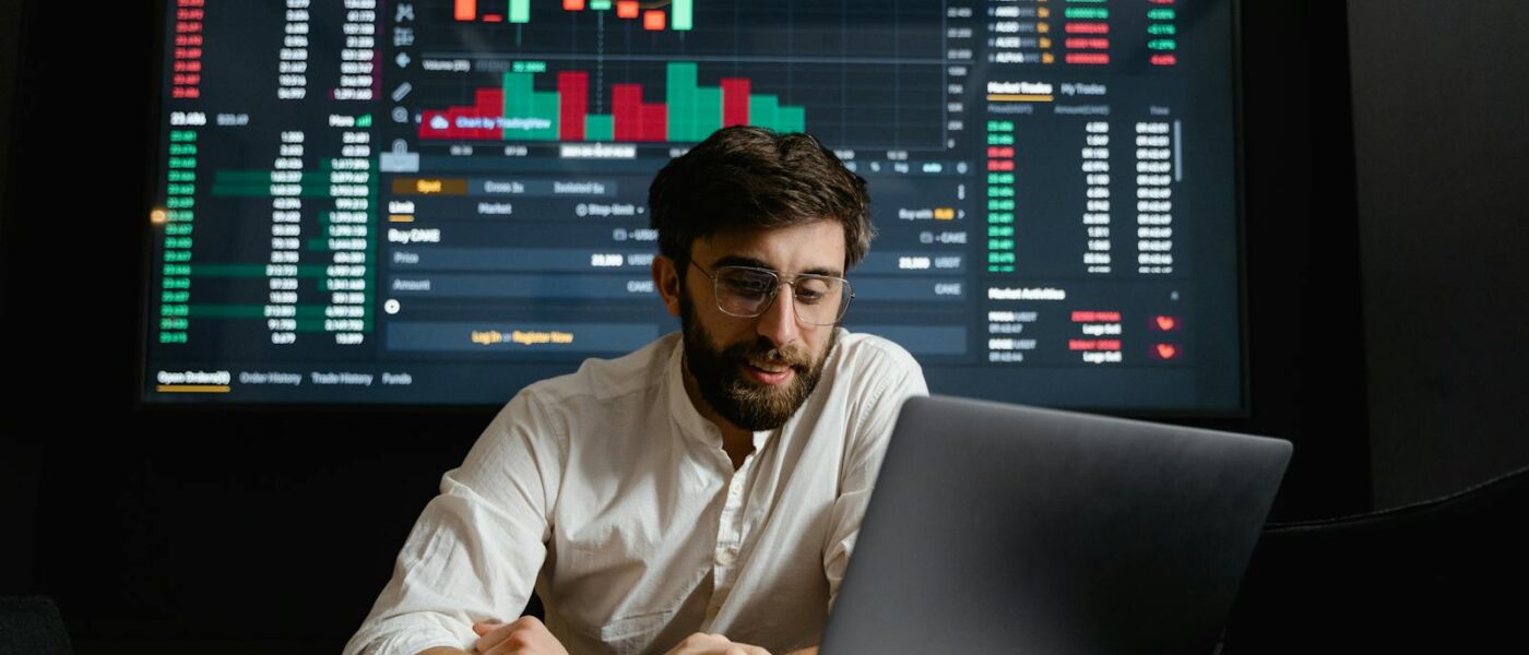 Male analyst studies cryptocurrency trends at a workstation with multiple displays showing market data.