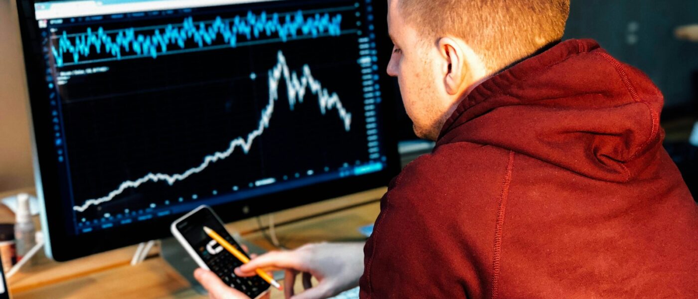 man holding black smartphone with flat screen monitor in front