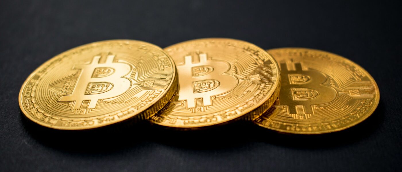 three gold-colored bitcoins on black surface