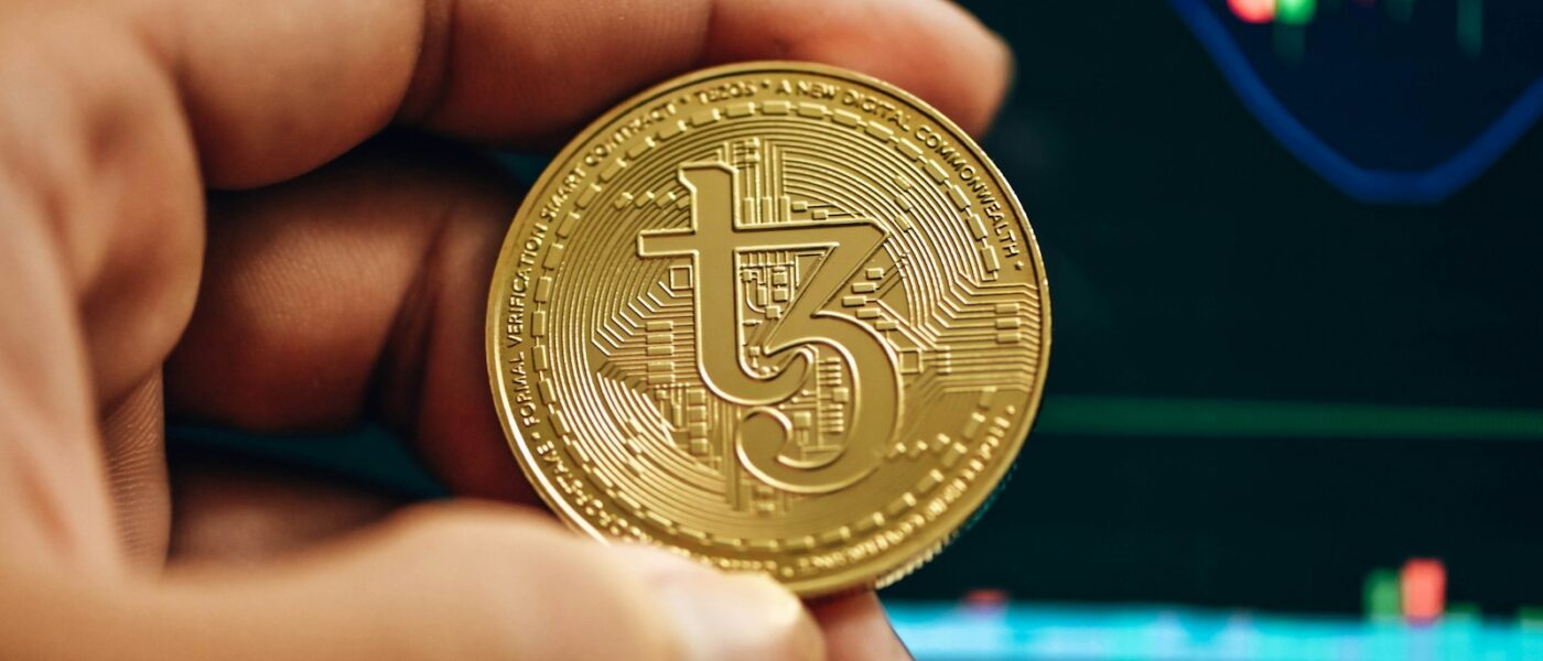 a hand holding a gold bitcoin in front of a stock chart